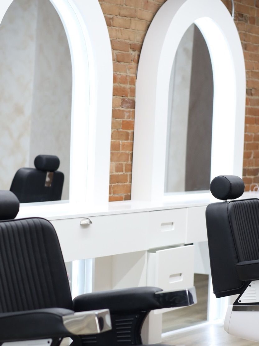 The row of barber chairs at One Up Barbers, with white arched mirror surrounds set into an exposed red brick wall.