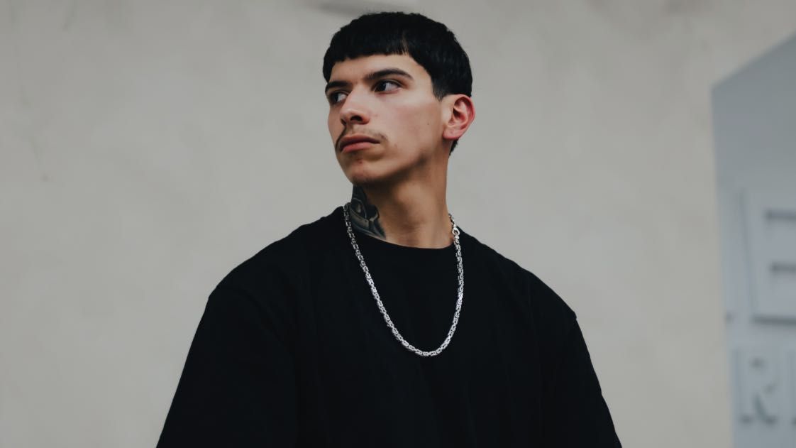 DVN1UP, photographed against the plaster wall in a black tee.