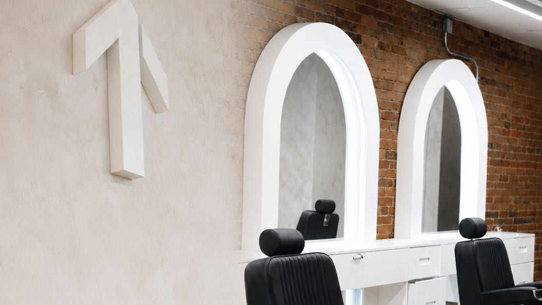 A white sculptural form mounted on the polished plaster wall, with two white arched mirror surrounds and exposed brick behind.